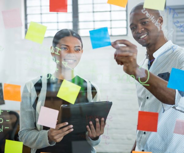 Business colleagues discussing over sticky notes on glass in office