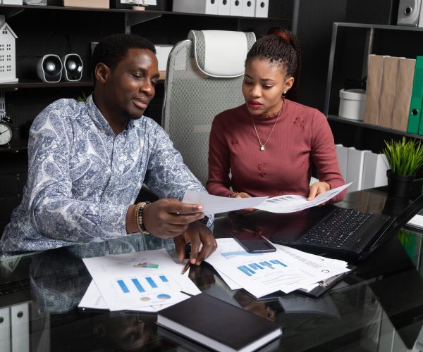 Various business colleagues sitting at table in modern office talking together. An African-American businessman and entrepreneur have an informal meeting in Cabinet. Two friendly black young men understand financial documents at Desk